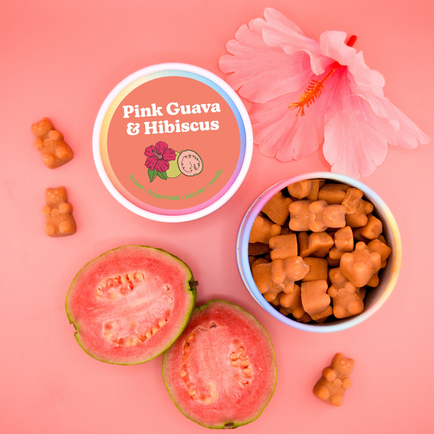 Pink wax melts in bear shapes displayed in a bowl with guava halves, hibiscus flower, and product lid on pink background.
