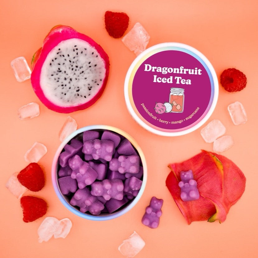 Purple wax melts in container with dragonfruit, label, ice cubes, and fresh dragonfruit on coral background.