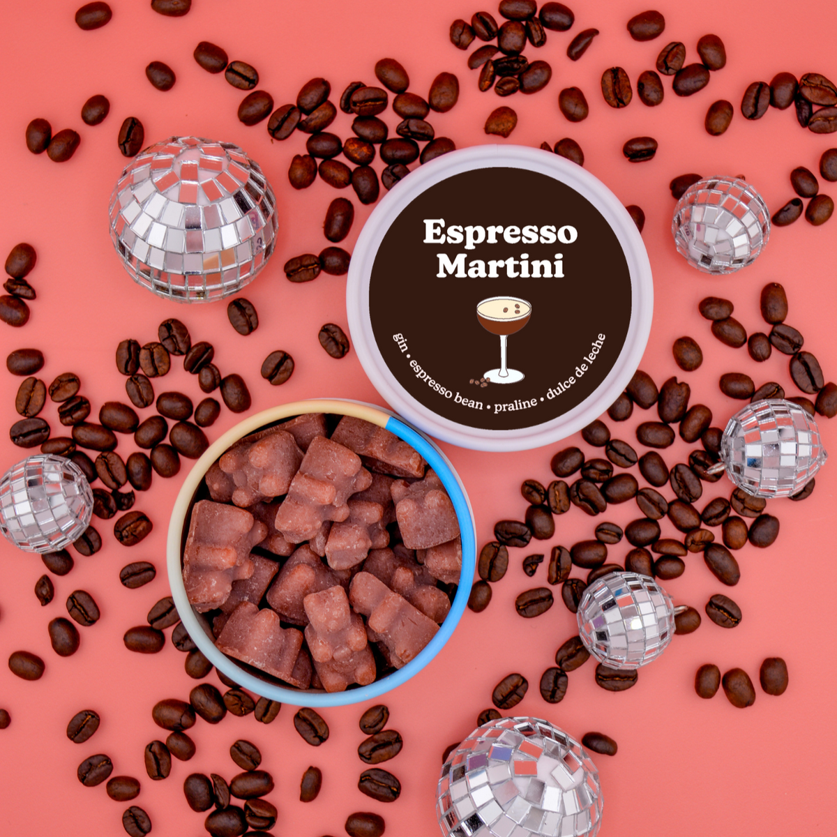 Brown wax melts in bowl with "Espresso Martini" label, coffee beans, and disco ball decorations on coral background.