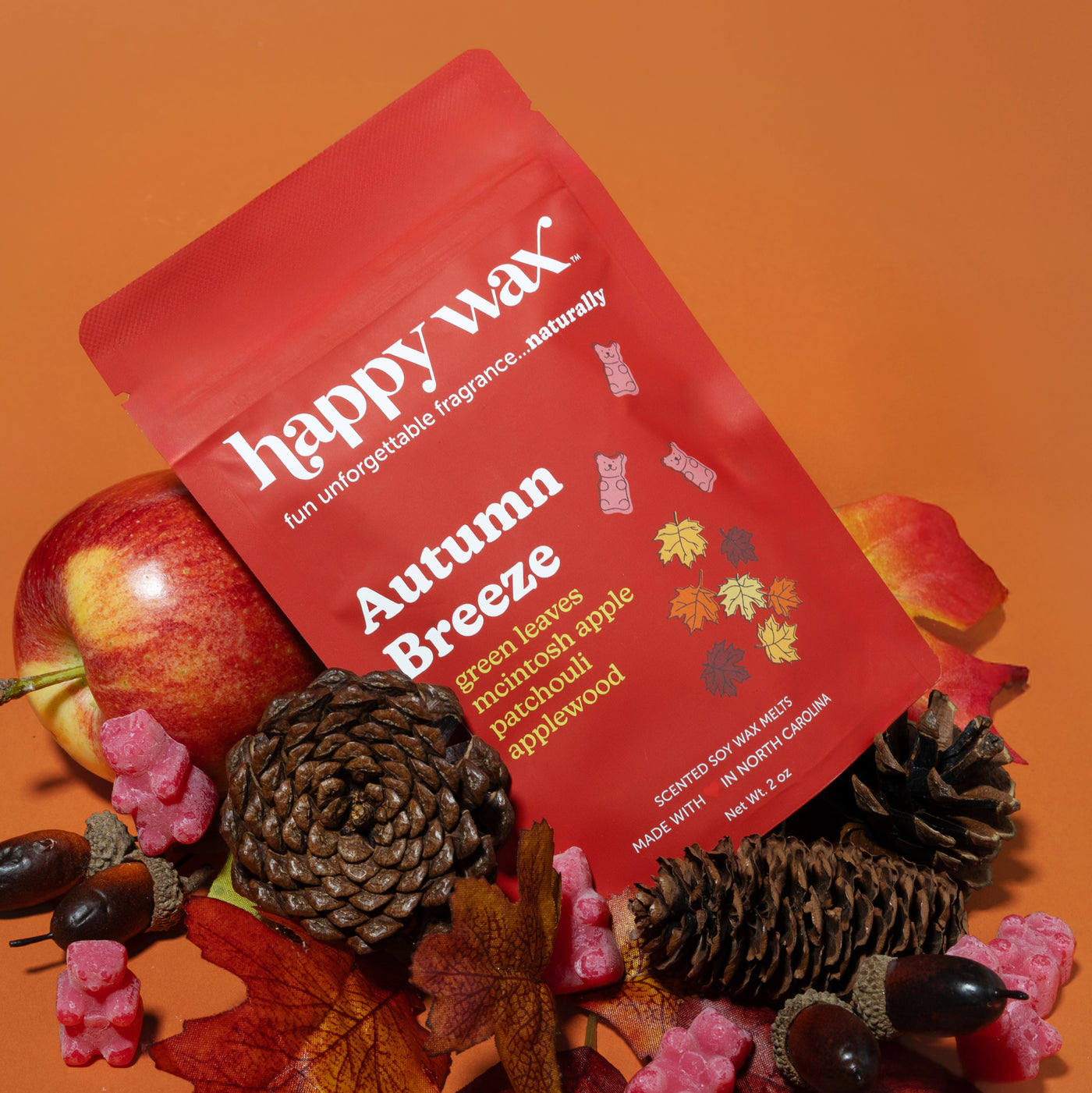 Red wax melt pouch labeled "Autumn Breeze" surrounded by apples, pinecones, and autumn leaves on orange background.