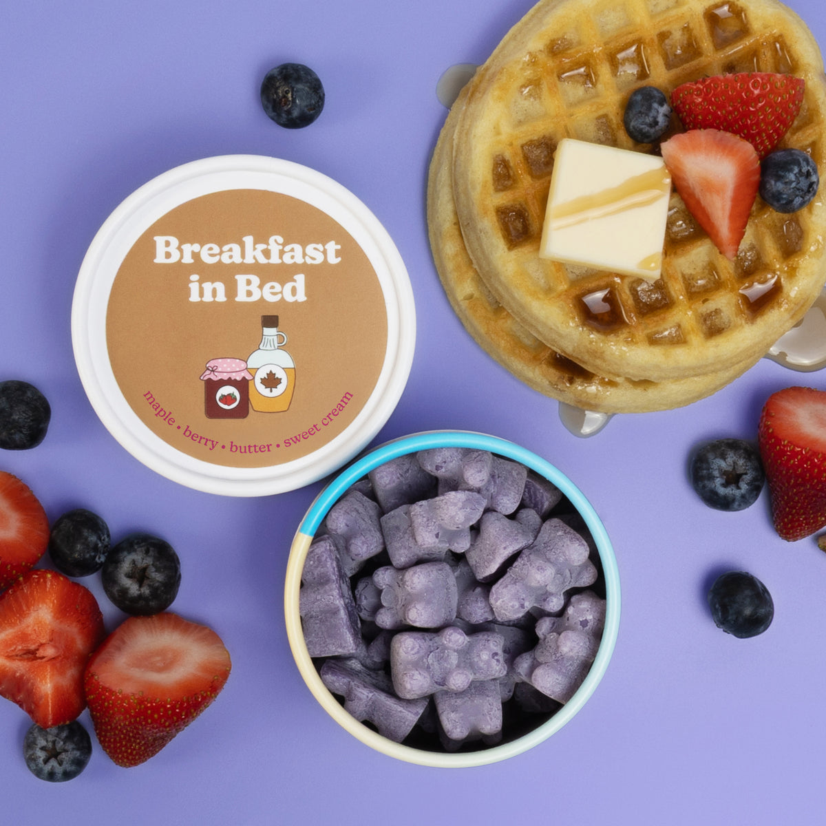 Wax melts in turquoise container with waffle, butter, berries, and scattered fresh strawberries and blueberries on purple bac