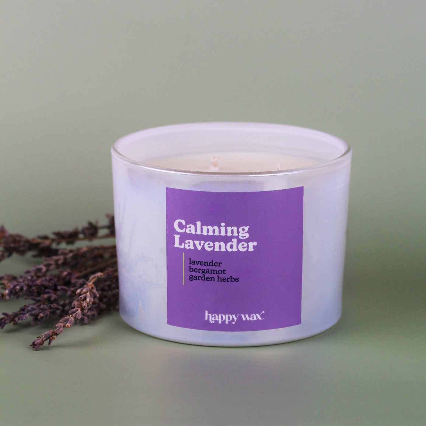 White three-wick candle with purple label reading "Calming Lavender" surrounded by dried lavender sprigs.
