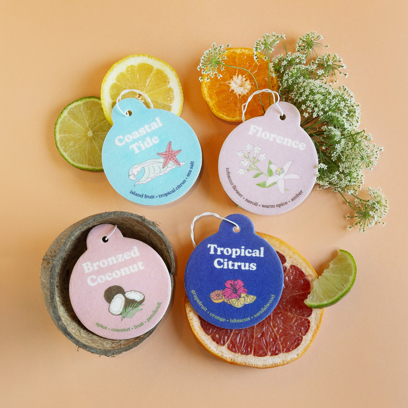 Four round scented car charms labeled Coastal Tide, Florence, Bronzed Coconut, and Tropical Citrus arranged with citrus slice