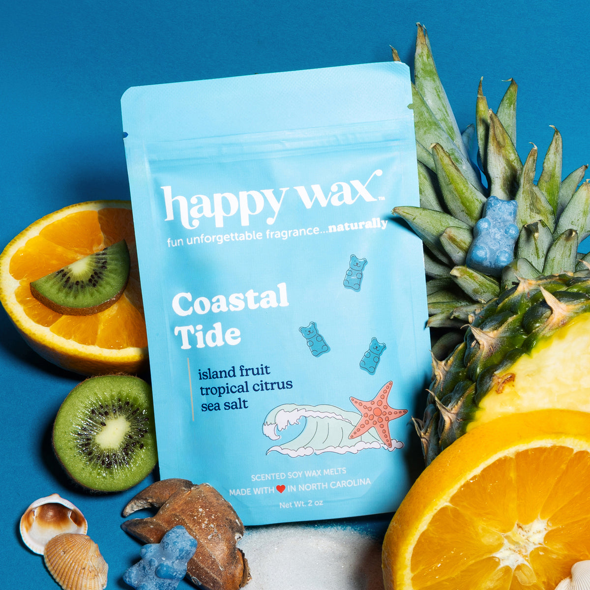 Light blue wax melt pouch surrounded by kiwi slices, orange segments, pineapple, shells, and starfish on blue background.