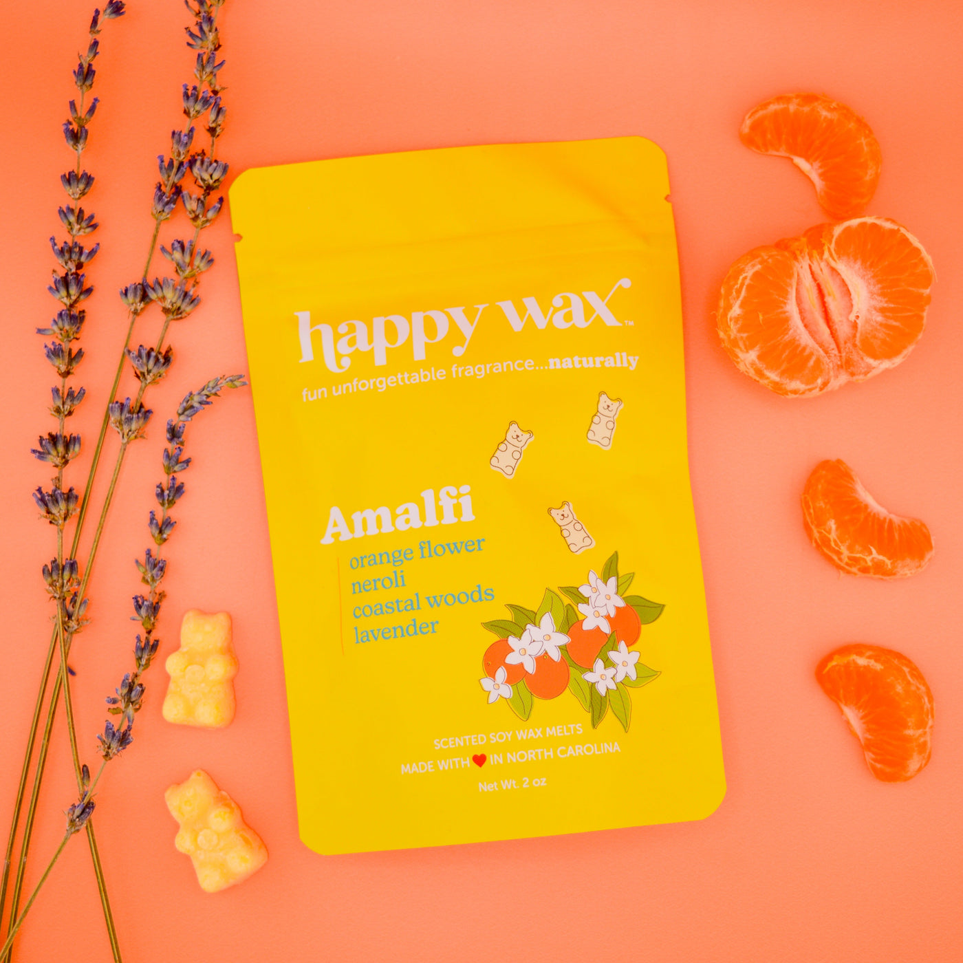 Yellow Happy Wax Amalfi wax melt pouch surrounded by dried lavender sprigs, fresh orange slices, and yellow wax melts on oran