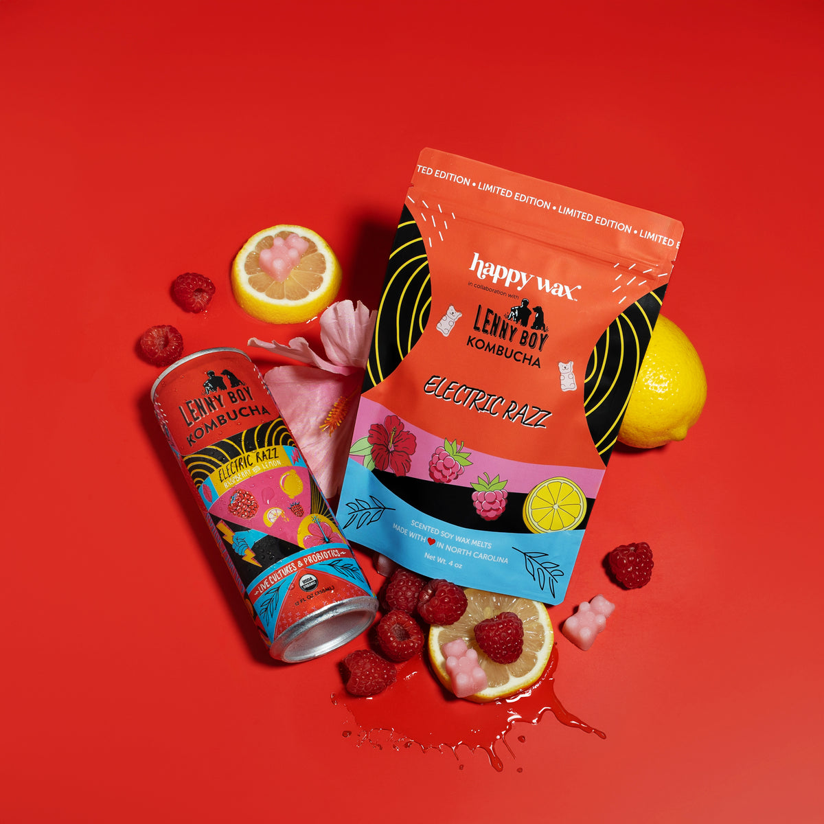 Colorful wax melt package and bottle with citrus slices, raspberries, and pink flowers on red background.