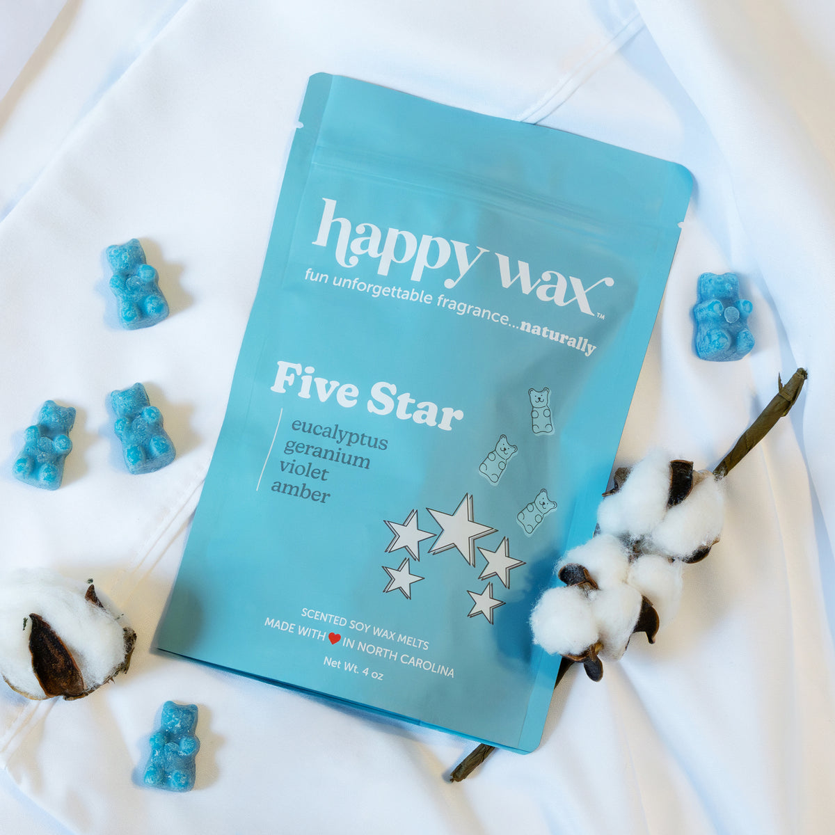 Turquoise pouch of Happy Wax Five Star soy wax melts surrounded by blue wax cubes and cotton stems on white background.