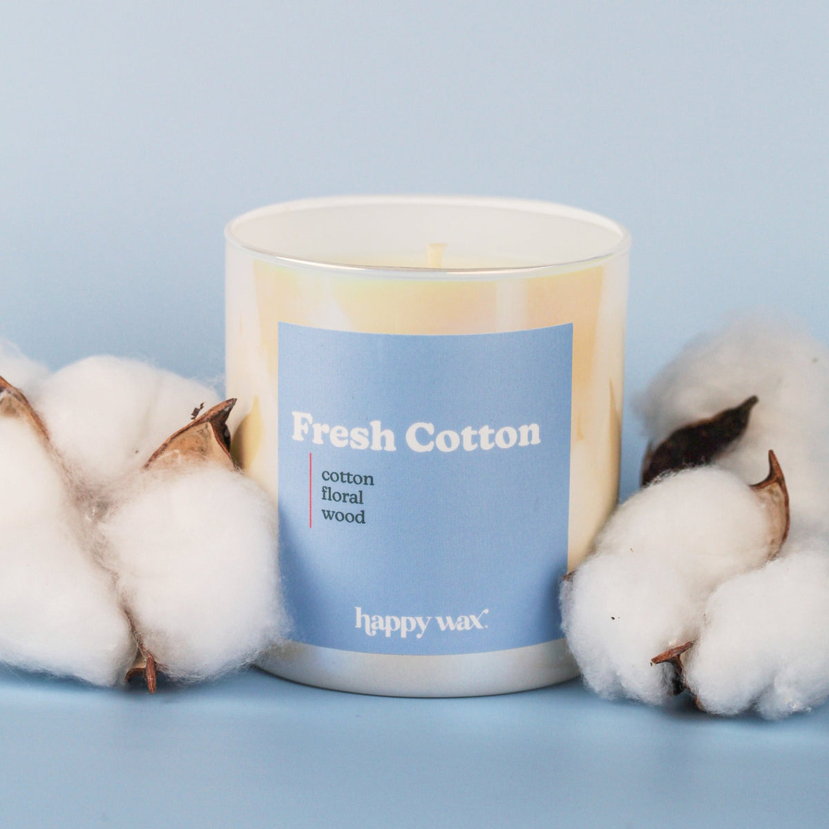 White cylindrical candle with blue label reading "Fresh Cotton" surrounded by cotton flowers on light blue background.