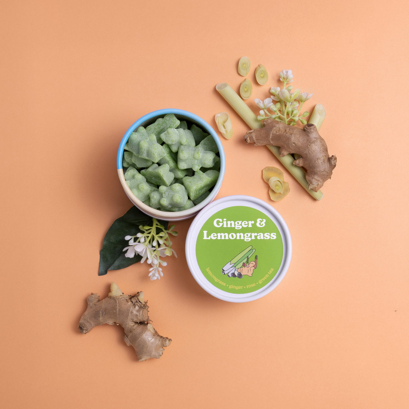 Blue and white container of pale green wax melts with labeled green lid, surrounded by ginger root and lemongrass sprigs on p