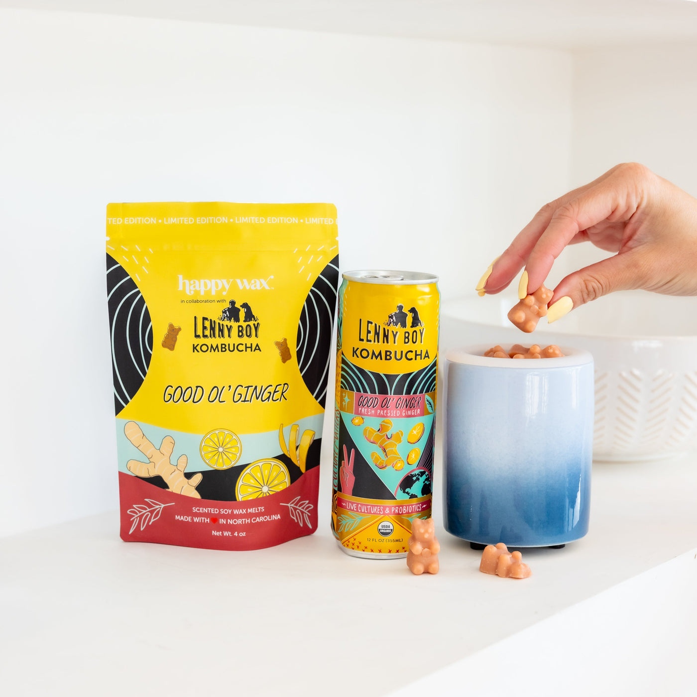 Yellow and blue wax melt package with ginger and lemon imagery, matching kombucha can, and white container with blue gradient