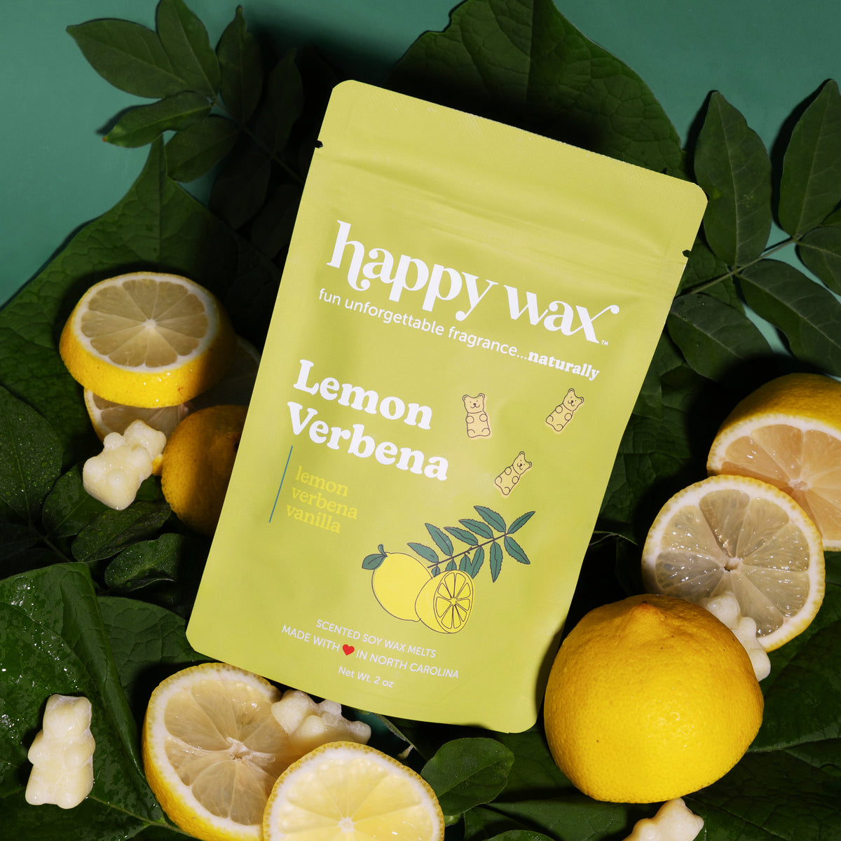 Yellow Happy Wax pouch of lemon verbena wax melts surrounded by fresh lemon slices, verbena leaves, and wax melt pieces.