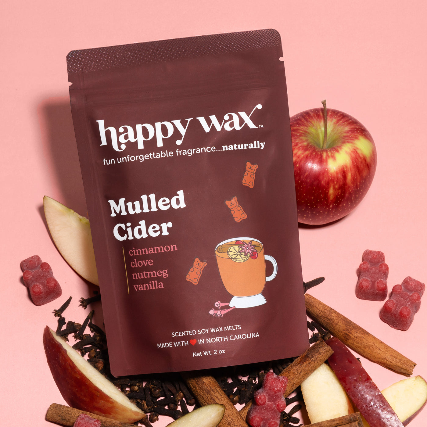 Dark brown pouch of Happy Wax mulled cider scented soy wax melts surrounded by apple slices, cinnamon sticks, and red wax mel