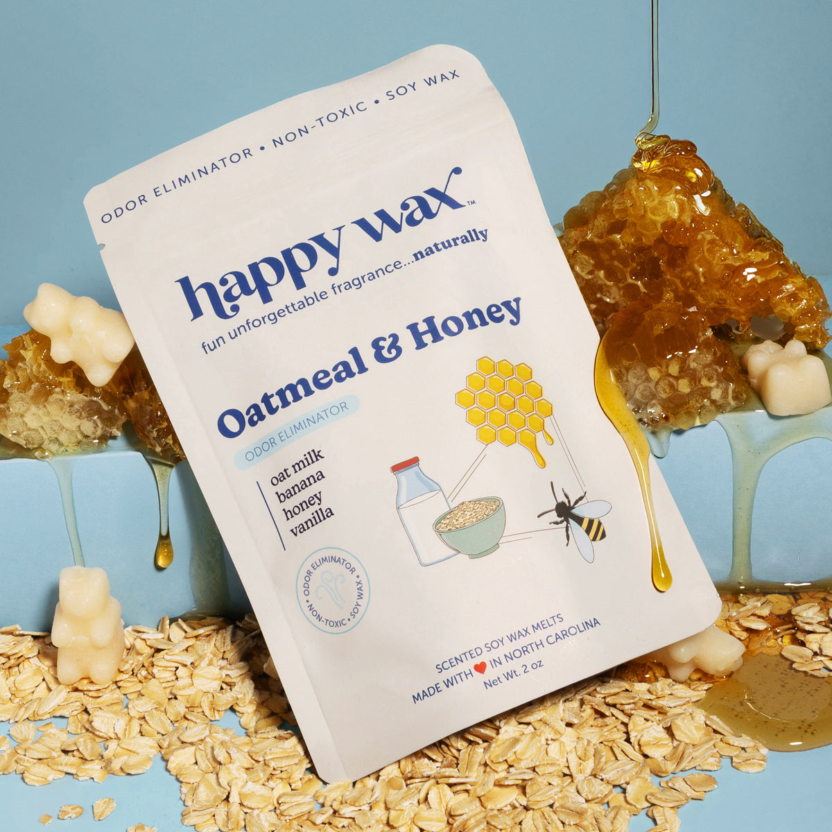 Cream-colored wax melt package with blue text surrounded by amber wax melts, oatmeal, honey dipper, and bee illustration on b