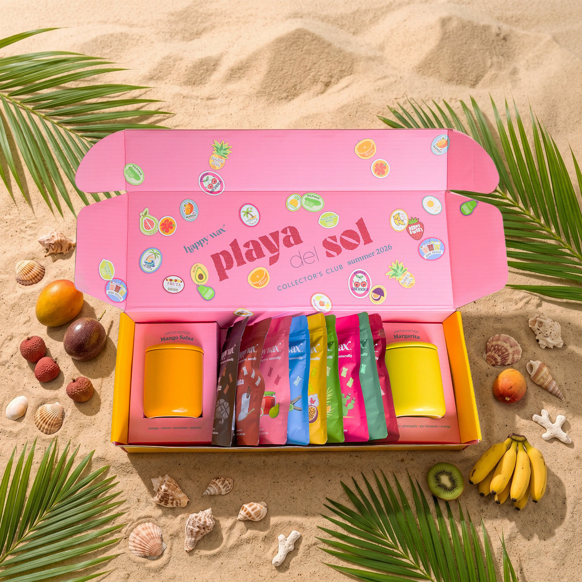 Pink 'playa del sol' subscription box on sand with tropical fruits and leaves