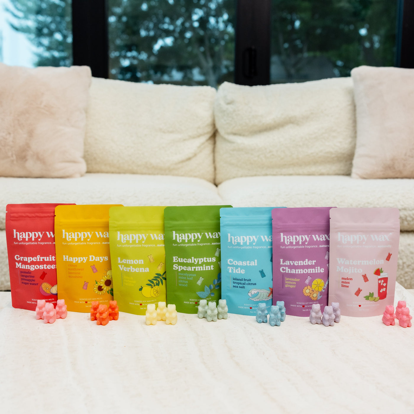 Seven colorful Happy Wax pouches in red, orange, yellow, green, blue, purple, and pink arranged with matching wax melts in fr