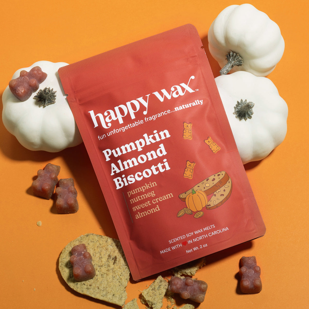 Happy Wax Pumpkin Almond Biscotti wax melts package surrounded by white decorative pumpkins and brown wax melt pieces on oran