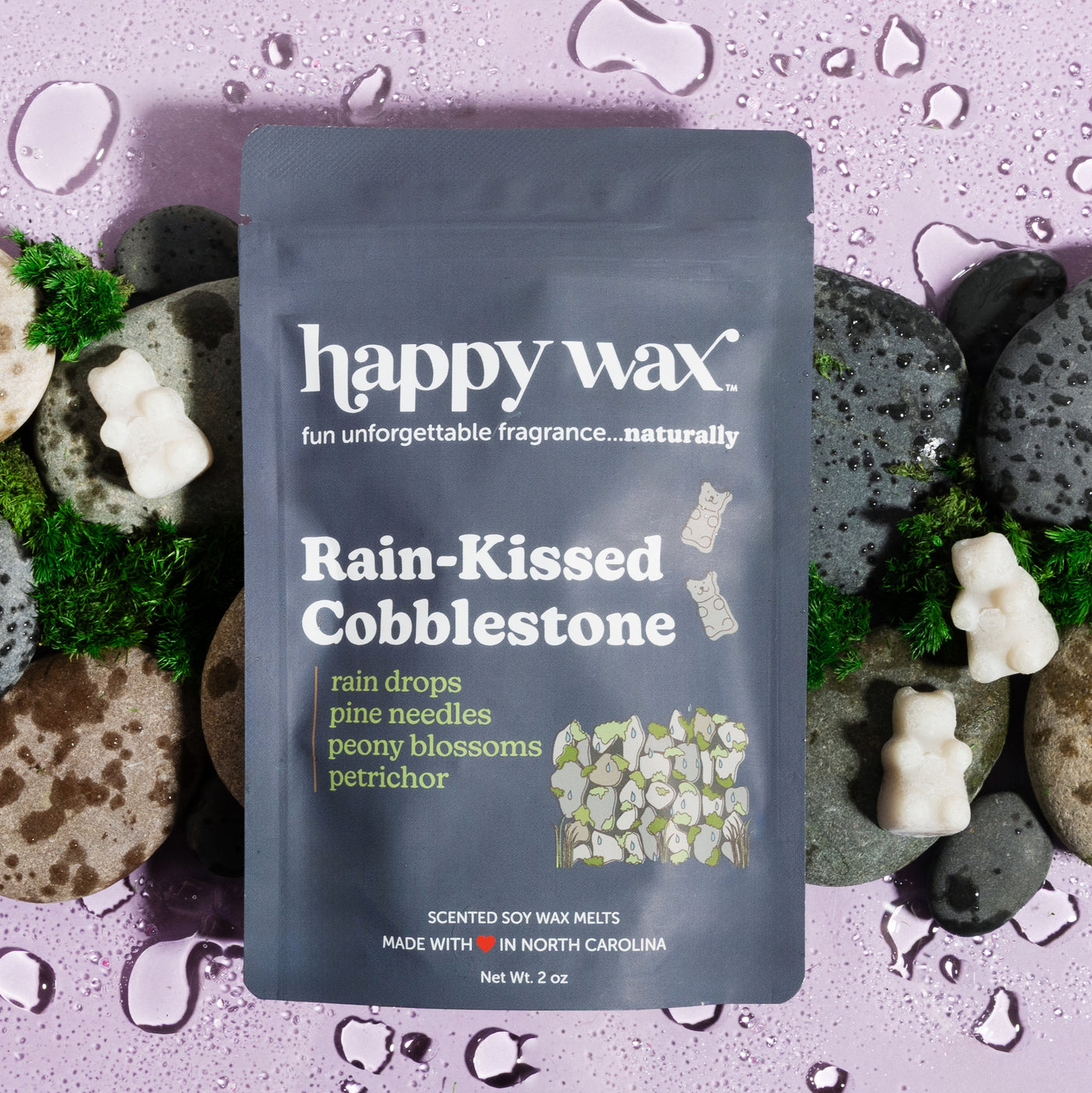 Dark blue pouch of happy wax soy wax melts surrounded by white wax melts, moss, and porous stones on purple speckled backgrou