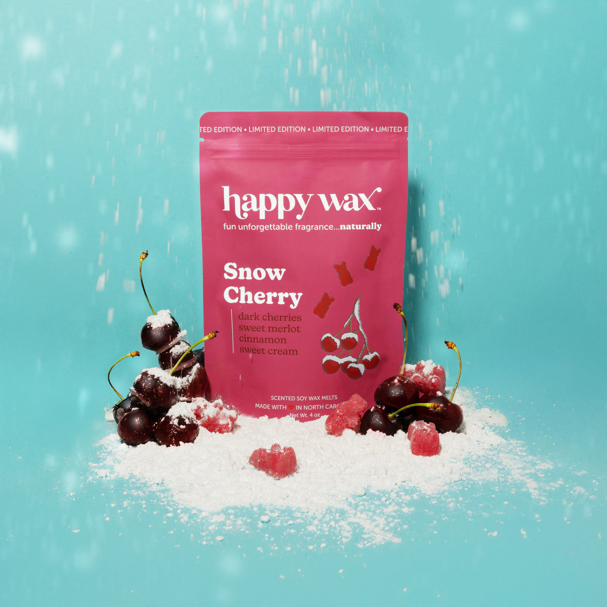 Pink Happy Wax pouch of Snow Cherry scented wax melts surrounded by fresh cherries and snow on turquoise background.