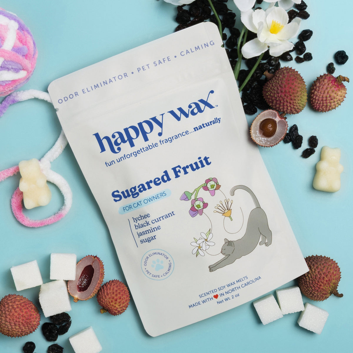 Happywax Sugared Fruit pet safe wax melts package surrounded by cream-colored wax melts, rambutan fruits, white flowers, and