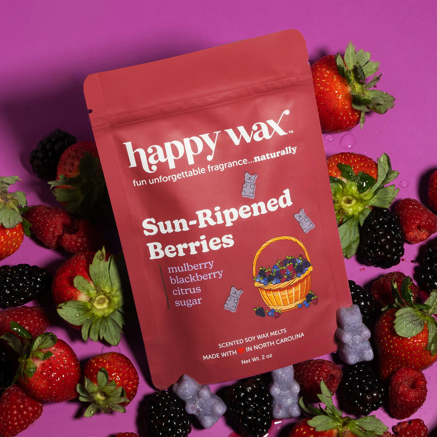Red Happy Wax pouch with Sun-Ripened Berries scent surrounded by fresh strawberries, blackberries, and purple wax melts on ma