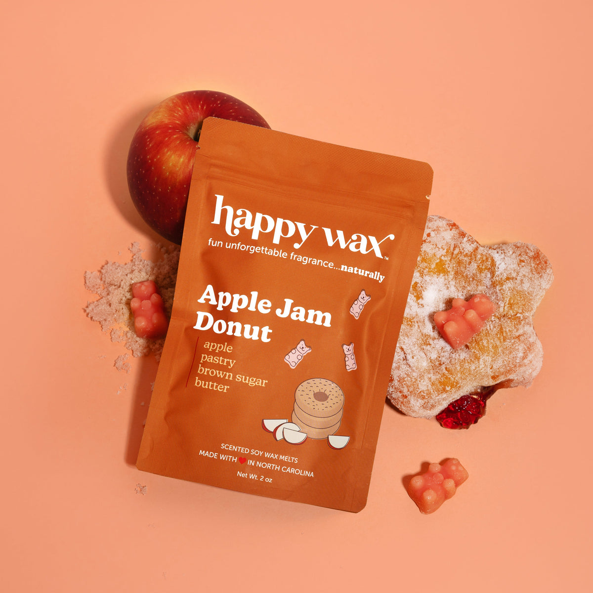 Orange Happy Wax pouch with Apple Jam Donut label surrounded by a red apple, sugar-coated donut, and red jam pieces on peach 