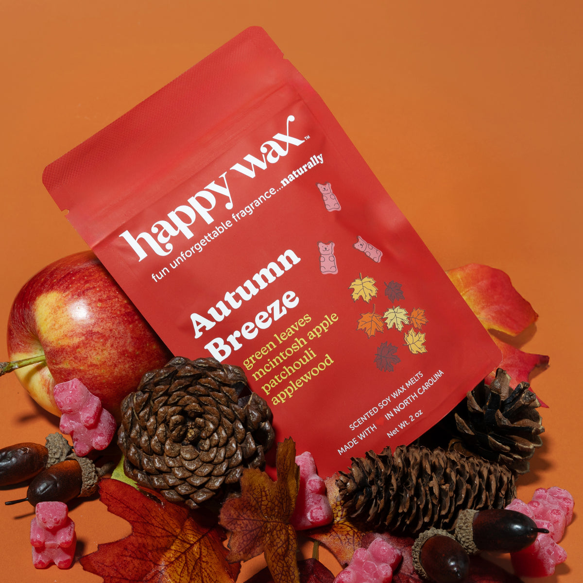 Red wax melt pouch labeled "Autumn Breeze" surrounded by apples, pinecones, and autumn leaves on orange background.