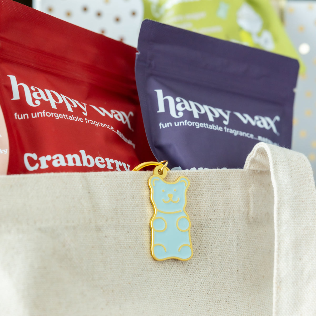 Light blue bear-shaped enamel keychain with gold outline and polka dot details attached to cream canvas pouch.