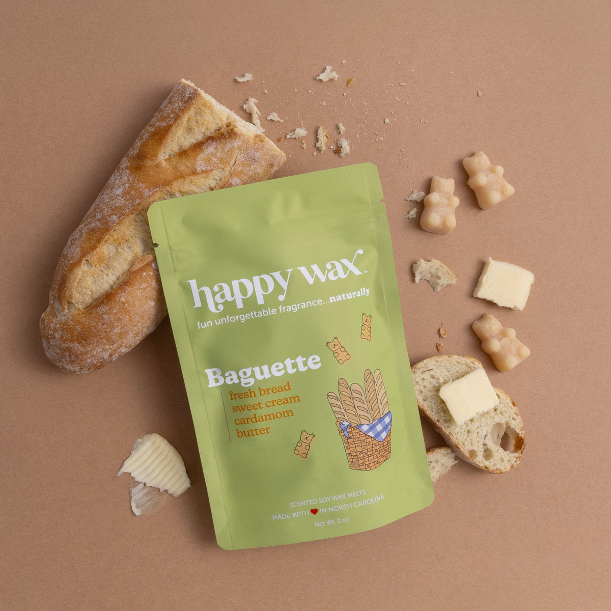 Green pouch of Happy Wax baguette-scented wax melts surrounded by bread slices, wax pieces, and butter on tan background.