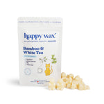 Cream-colored wax melts next to a white pouch labeled "Happy Wax Bamboo & White Tea" with cat and tea cup illustrations.