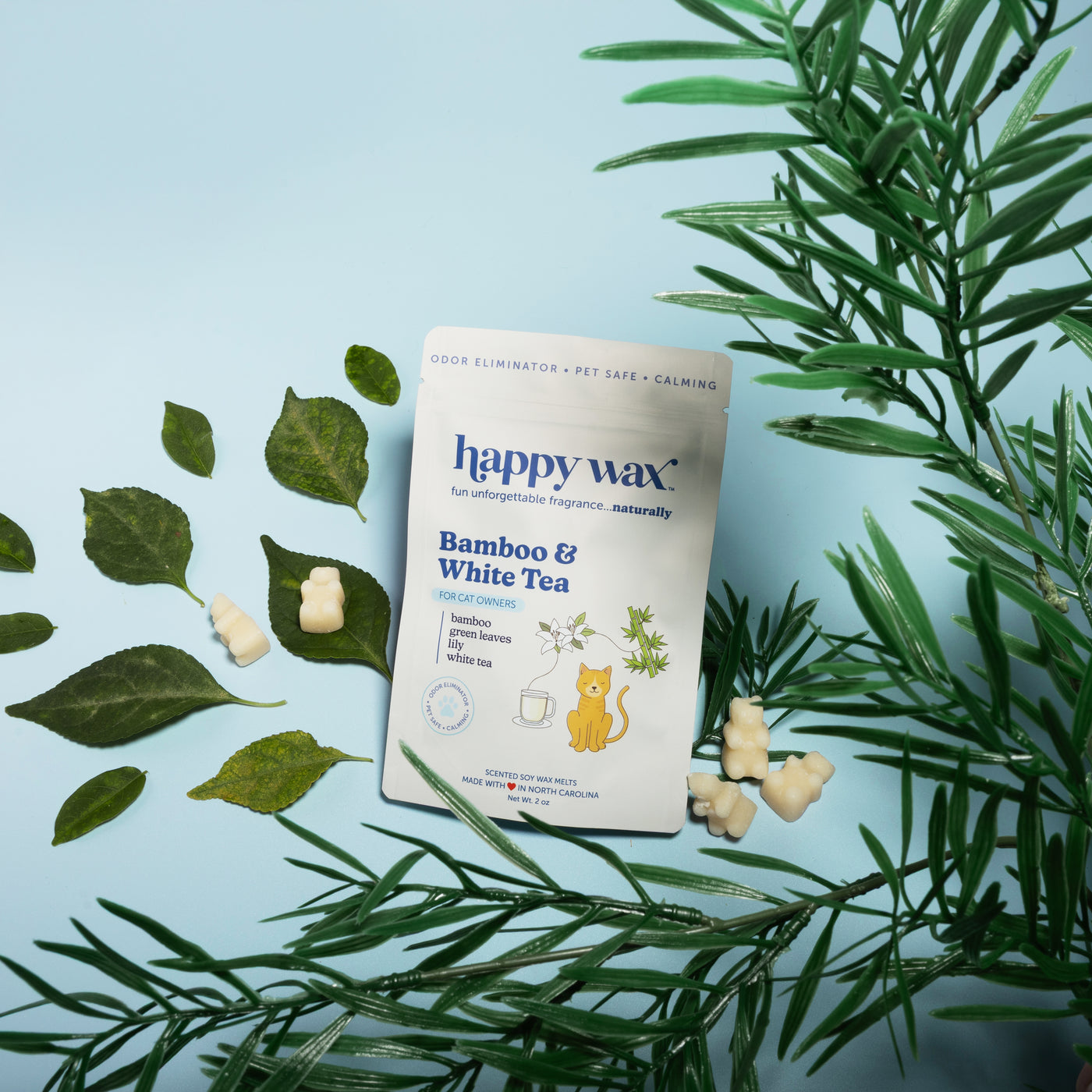 Happy Wax bamboo and white tea pet wax melts package with cream-colored melts and green plant leaves on light blue background