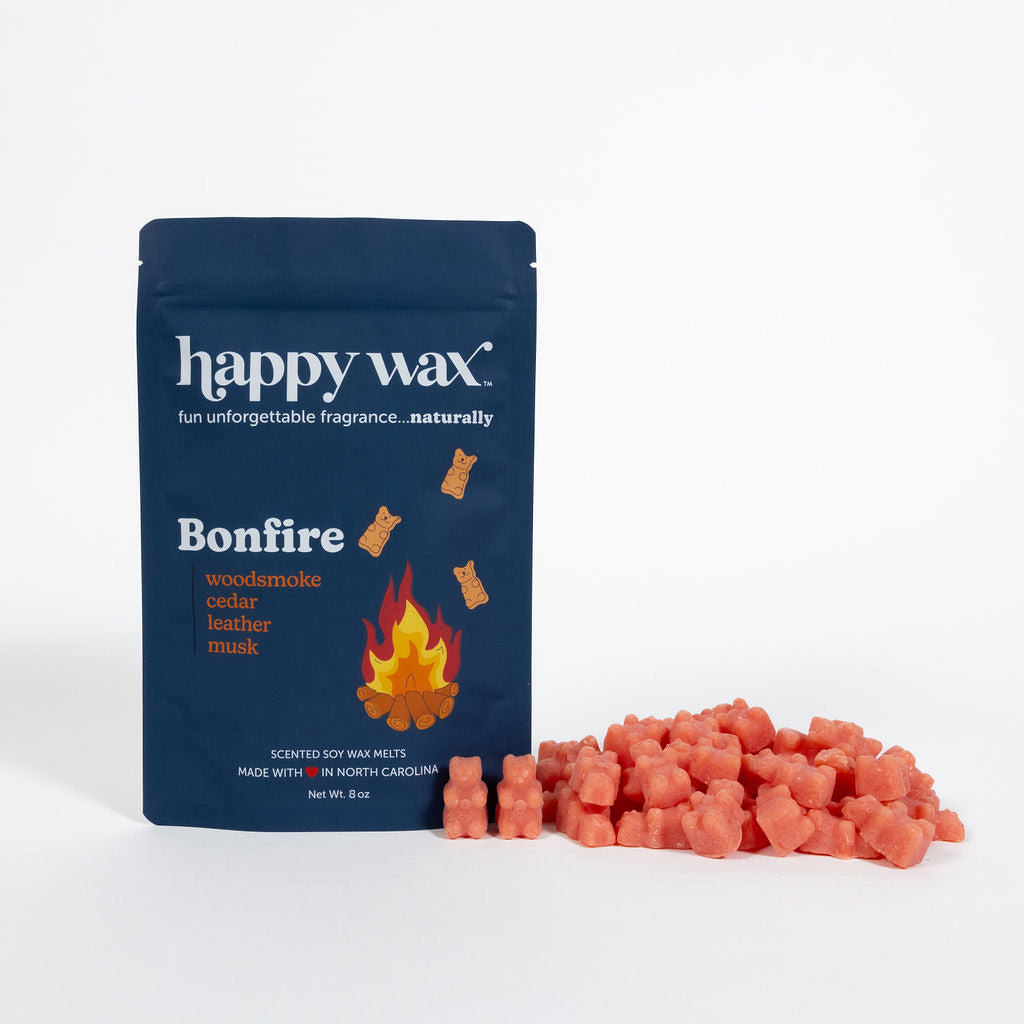Dark blue pouch of Happy Wax Bonfire scented wax melts with coral-colored wax chunks displayed beside it.