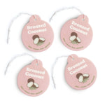 Four pink round car charms with "Bronzed Coconut" text, coconut illustrations, and scent descriptors, each with a white strin
