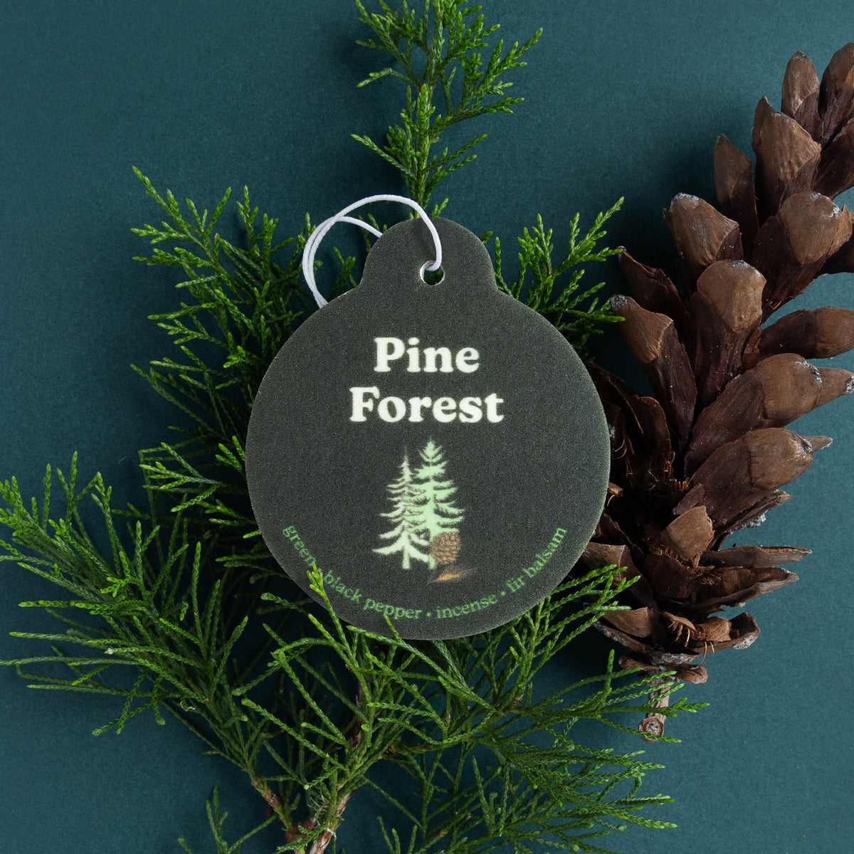 Dark gray round car charm with white metal loop, displaying "Pine Forest" text and tree illustration, surrounded by fresh pin