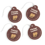 Four brown leather round charms with gold wheat design, white text, and white string attachments.