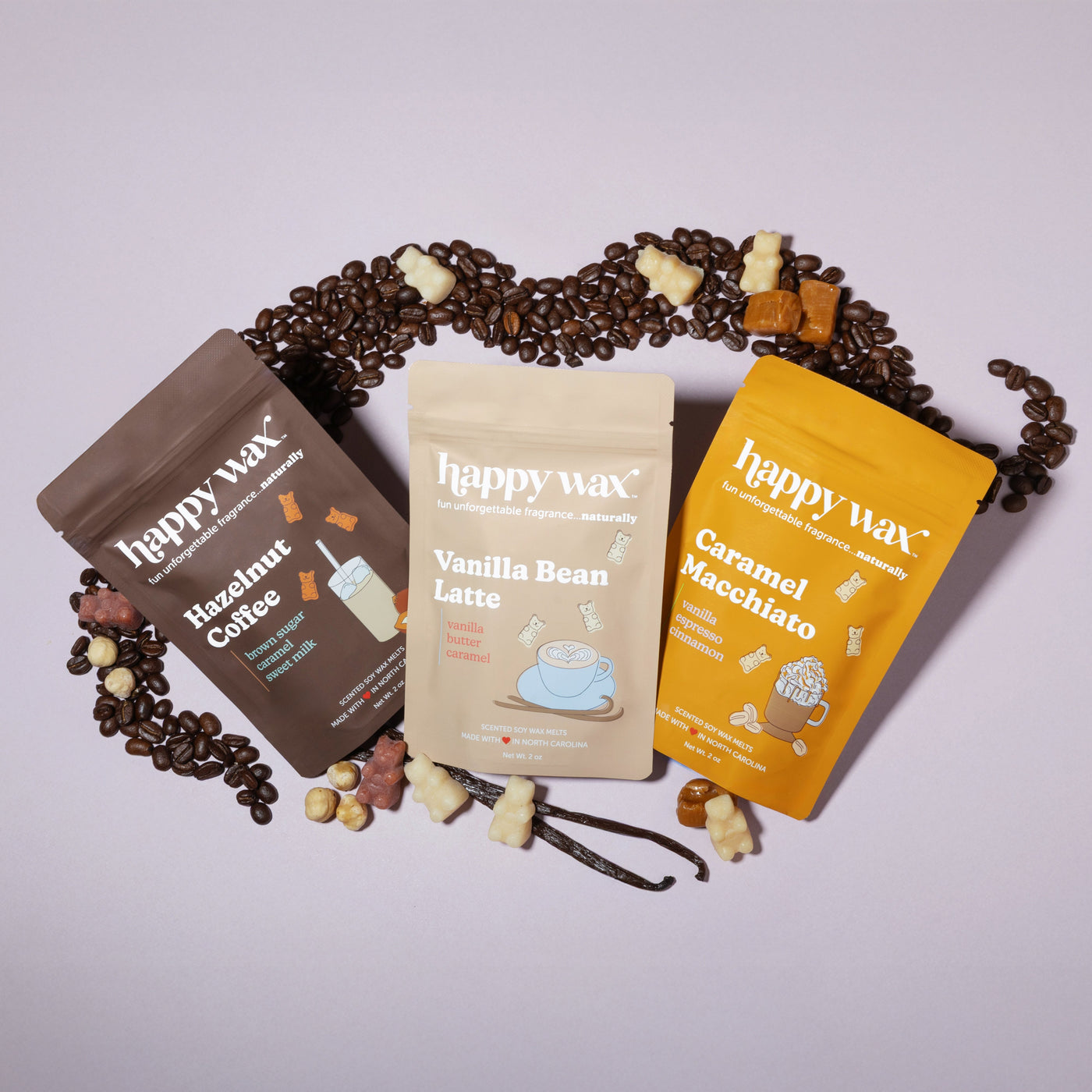 Three Happy Wax fragrance pouches in brown, cream, and yellow labeled Hazelnut Coffee, Vanilla Bean Latte, and Caramel Macchi