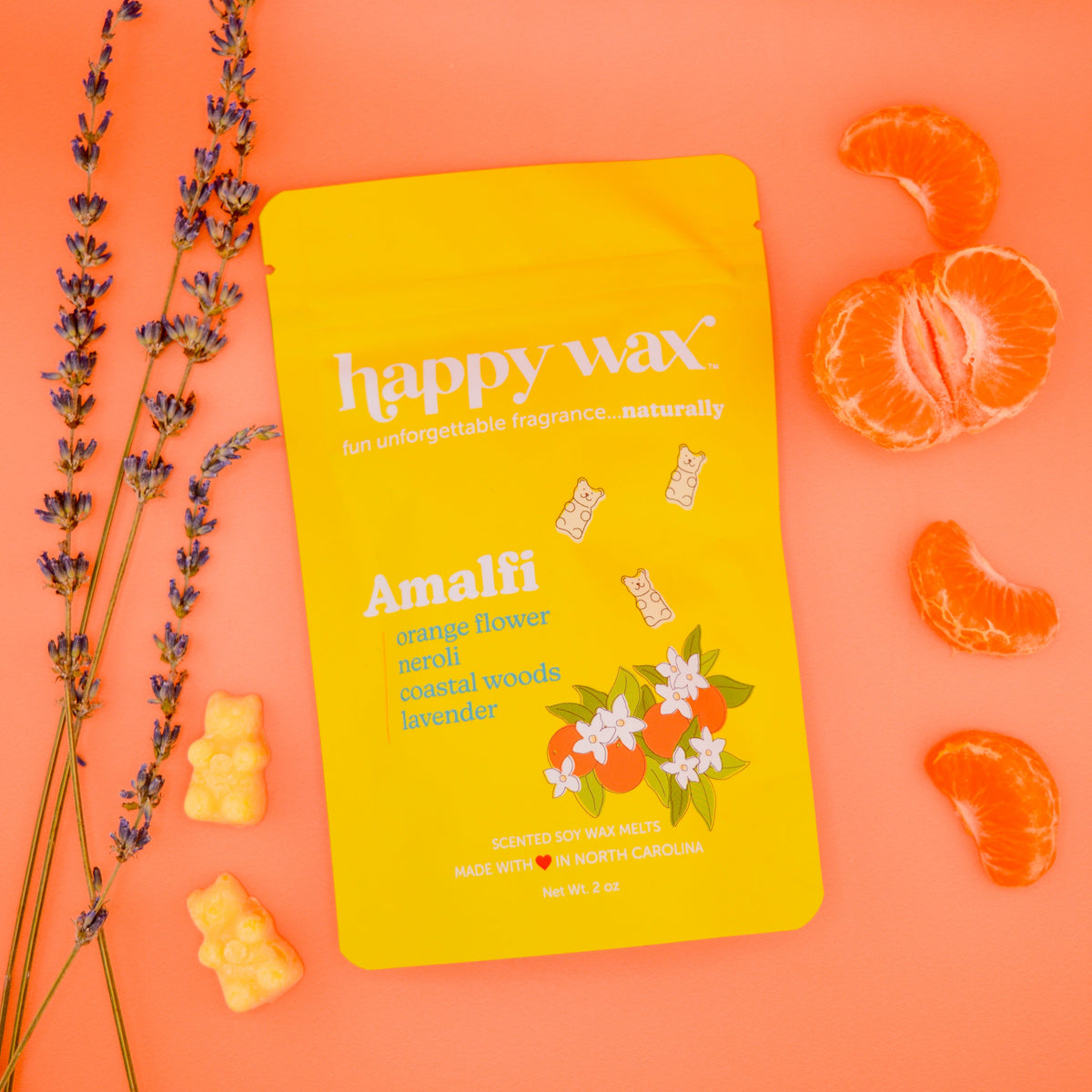 Yellow Happy Wax Amalfi wax melt pouch surrounded by dried lavender sprigs, fresh orange slices, and yellow wax melts on oran