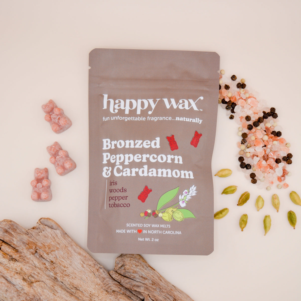 Happy Wax Bronzed Peppercorn & Cardamom soy wax melts in taupe pouch surrounded by pink and brown wax pieces, cardamom pods, 
