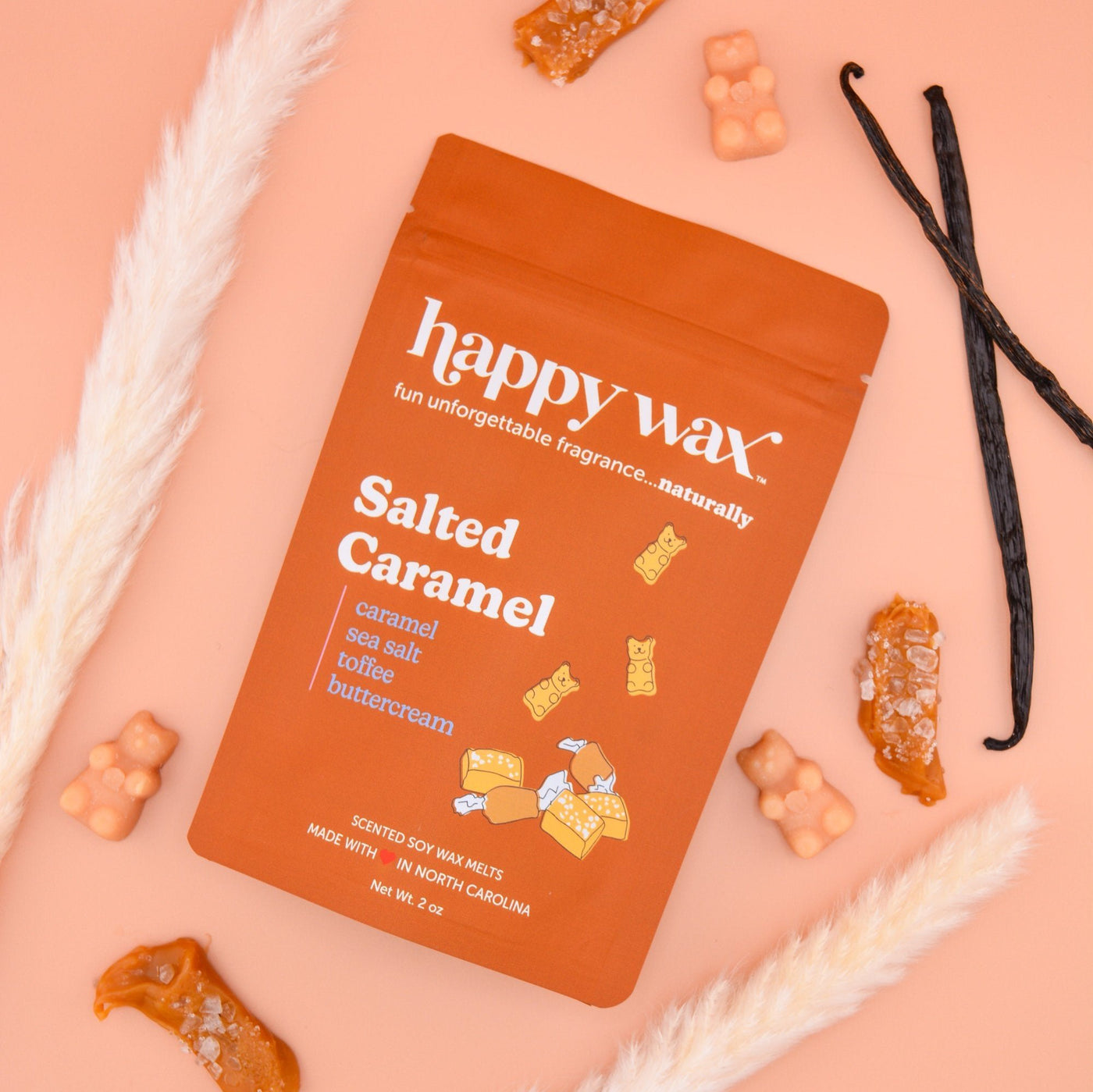 Orange Happy Wax Salted Caramel wax melts package surrounded by vanilla beans, white feathers, and caramel-colored wax pieces