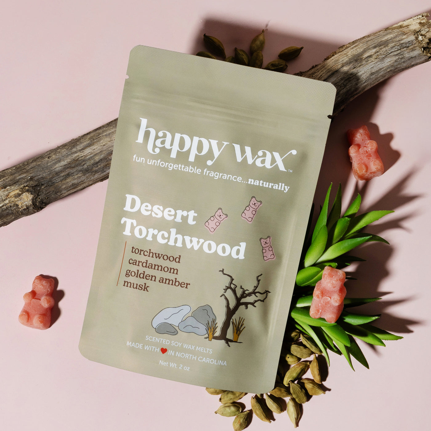 Pale green pouch of Happy Wax Desert Torchwood wax melts surrounded by dried botanicals and coral-colored wax bear shapes on 