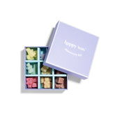 Lavender box containing nine wax melts in various colors including yellow, green, cream, pink, and brown arranged in compartm