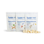 Three Happy Wax pouches labeled Teakwood Trail, Lavender Field, and Almond Blossom with scattered wax melts in front.
