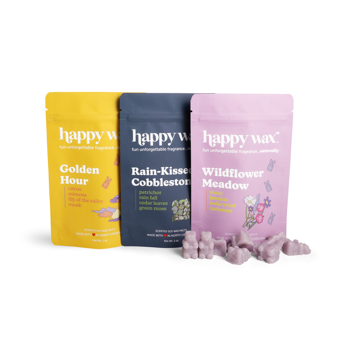 Three scented wax melt pouches in yellow, charcoal, and pink with scattered lavender-colored wax melts in front.