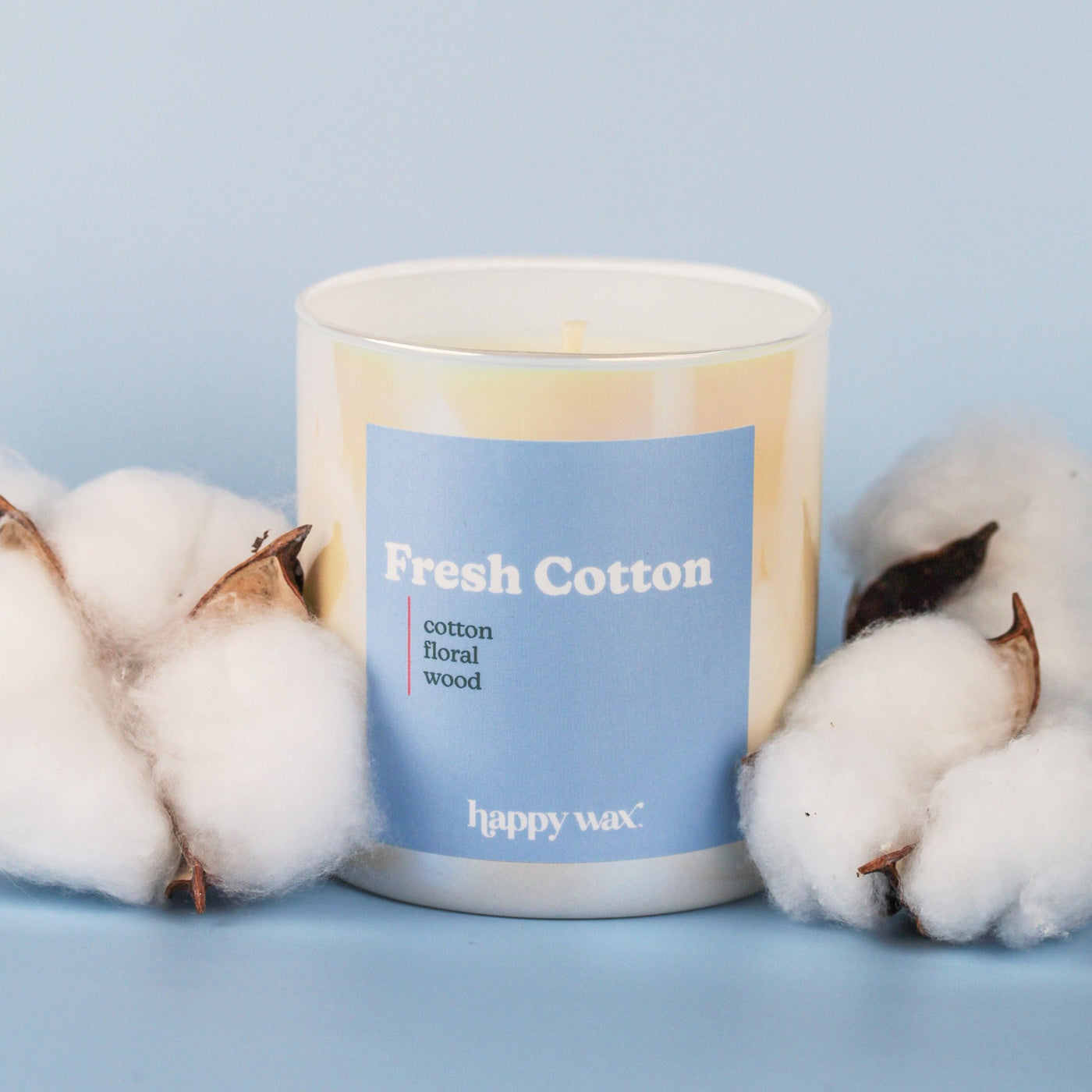 White cylindrical candle with blue label reading "Fresh Cotton" surrounded by cotton flowers on light blue background.