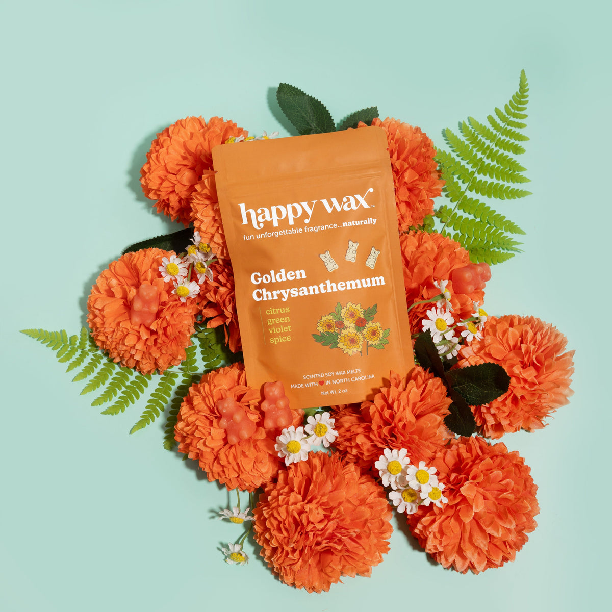 Orange Happy Wax package of Golden Chrysanthemum wax melts surrounded by orange chrysanthemums, small white flowers, and gree
