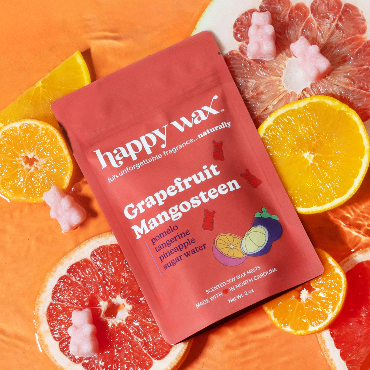 Red pouch of Happy Wax grapefruit mangosteen wax melts surrounded by grapefruit halves, orange slices, and pink wax melts.