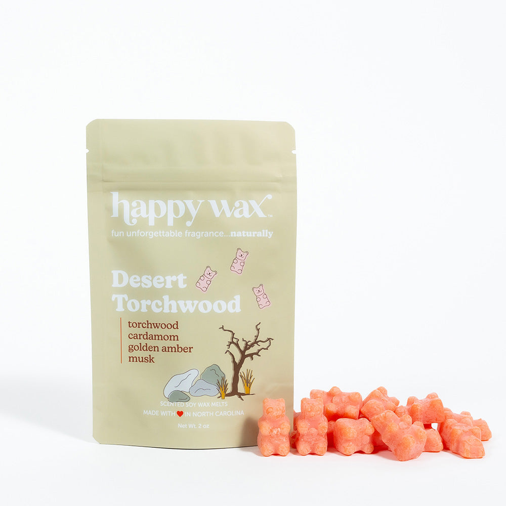 Cream-colored Happy Wax pouch with Desert Torchwood label next to pile of coral-pink wax melts.