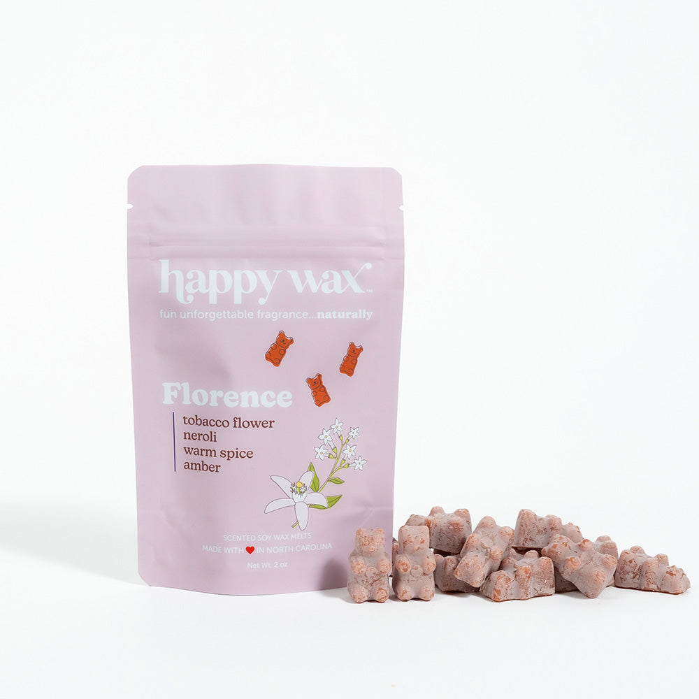 Pink pouch of Happy Wax Florence wax melts with scattered tan-colored wax pieces beside it.
