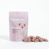Pink pouch of Happy Wax Florence wax melts with scattered tan-colored wax pieces beside it.