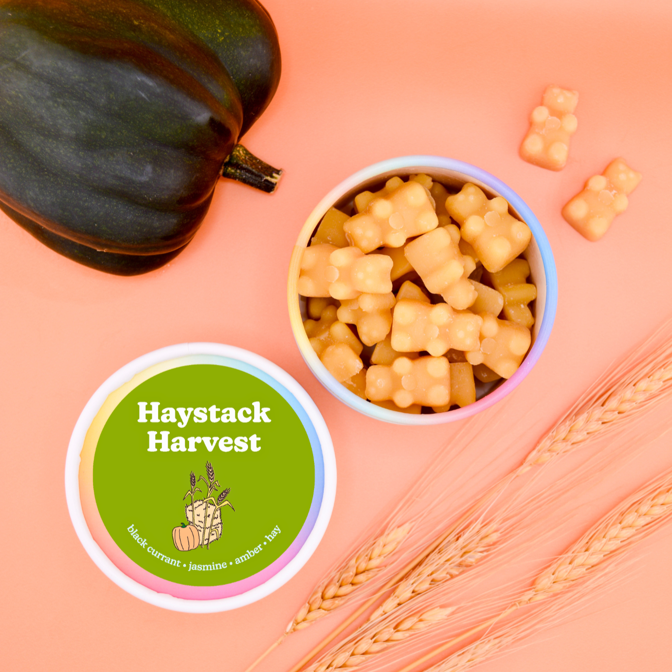 Haystack Harvest wax melts in a white and pink container with green label, peach-colored melts in bowl, dried wheat, and eggp