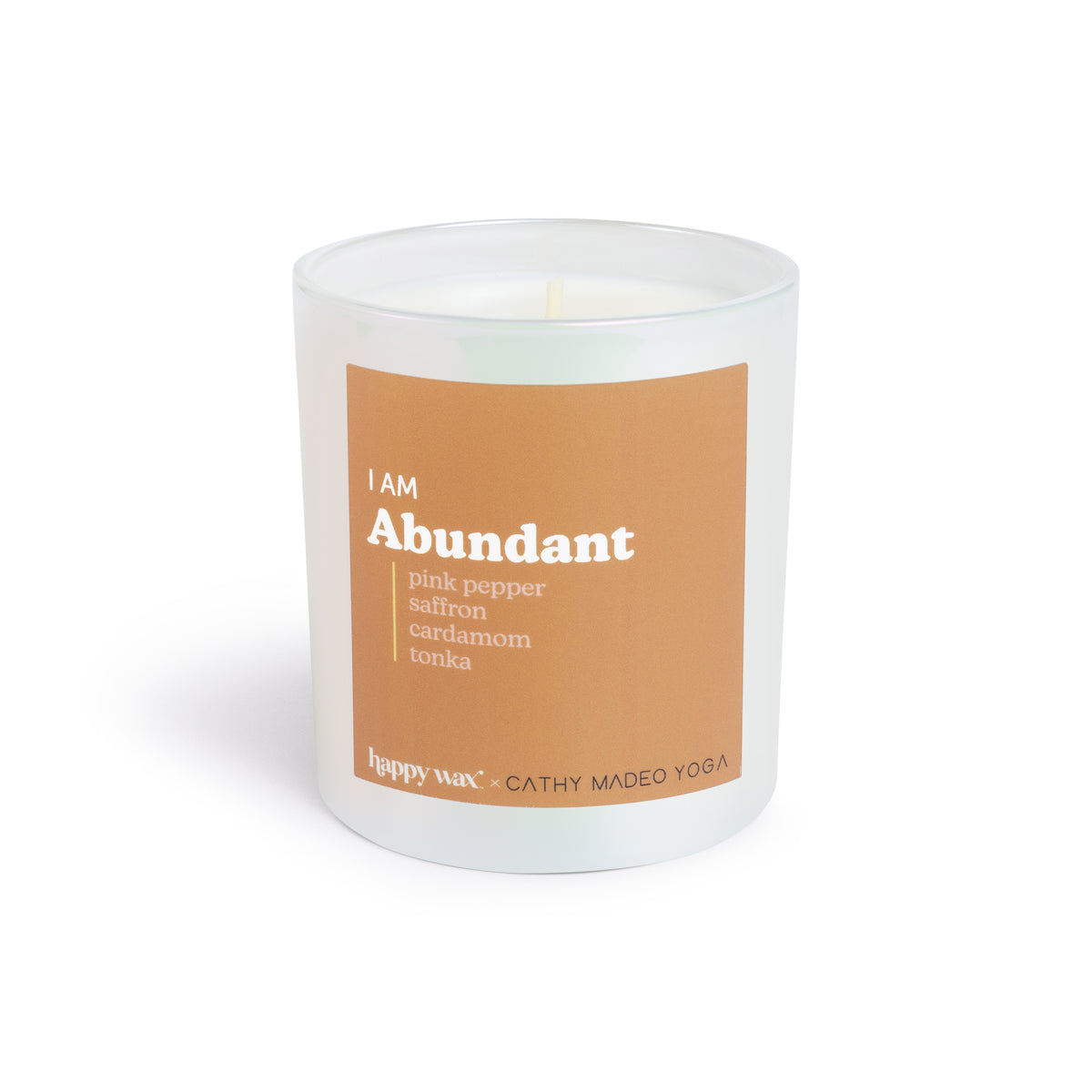 White cylindrical candle with tan label reading "I AM Abundant" and scent notes including pink pepper, saffron, cardamom, and
